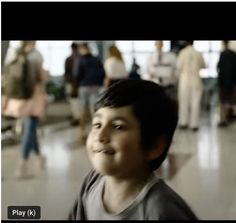 a young boy standing in an airport looking at the camera with people walking around him