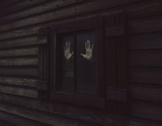 two hands are seen through the window of a wooden house, with only one hand visible