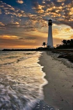 a light house sitting on top of a sandy beach next to the ocean at sunset