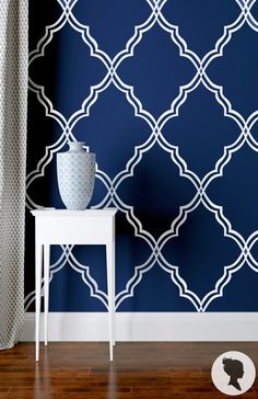 a white table sitting next to a blue wall with a vase on top of it