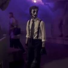 a man wearing a clown mask and tie standing in front of a purple light with other people