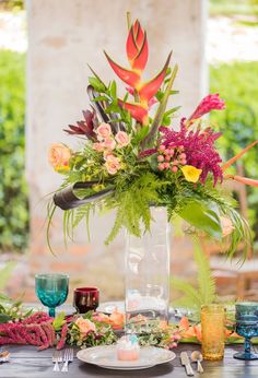 an arrangement of flowers and greenery in a vase on top of a wooden table