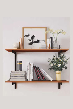 two wooden shelves with books, vases and pictures on them against a white wall