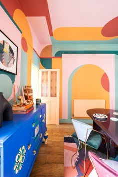 a room with colorful walls and furniture in the center, including a blue chest of drawers