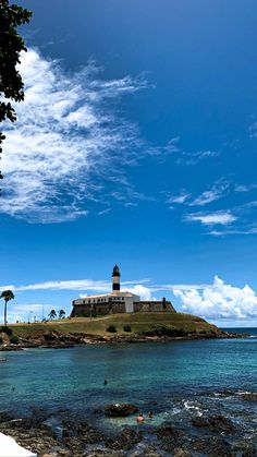 an island with a light house on top and people swimming in the water near it