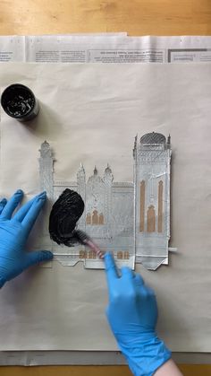 two hands in blue gloves are painting on a piece of white paper with black paint