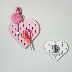 two heart shaped magnets with scissors attached to them on a white surface next to a pink wall hook