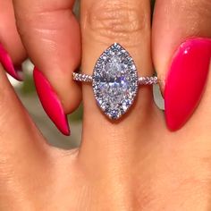 a woman's hand with pink nail polish holding a diamond ring and two fingers