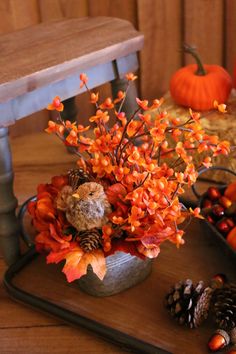 an arrangement of fall flowers and pine cones on a table with other autumn decorations in the background