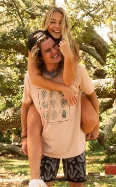 a man holding a woman on his back in front of a tree and grass area