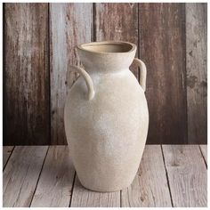 a large white vase sitting on top of a wooden table next to a wood wall