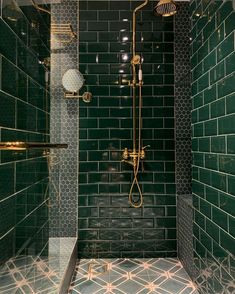 a green tiled bathroom with gold fixtures and glass shower head in the corner, along with black tiles on the walls