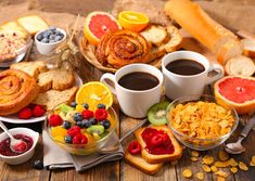 two cups of coffee are next to some fruit and bread on a table with other foods