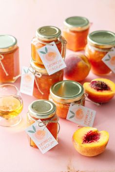 peach jam in jars with labels on them sitting on a pink surface next to some fruit