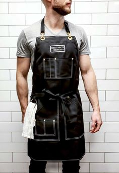 a man wearing an apron standing in front of a white brick wall