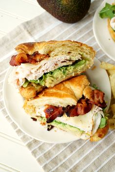 two white plates with sandwiches and chips on top of a table next to an avocado