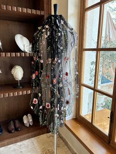 an umbrella with flowers on it sitting in front of a book shelf next to a window