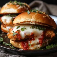 two chicken parmesan sandwiches on a black plate with fresh herbs and cheese, ready to be eaten