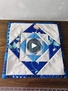 a blue and white quilted square with a circular design on the center, sitting on top of a wooden table