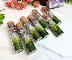 six glass tubes filled with different types of flowers on a white marble counter top next to pink and purple flowers