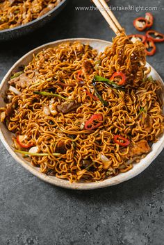 a bowl full of noodles with chopsticks in it and another bowl behind it