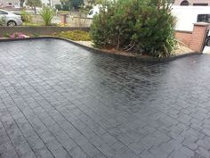 a black paved driveway with trees and bushes in the backgroung, next to a brick wall