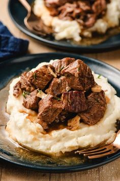 two plates filled with mashed potatoes and beef on top of each other next to a fork