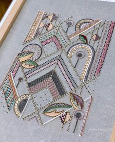 an embroidered piece is displayed in a frame on the table, with beads and thread