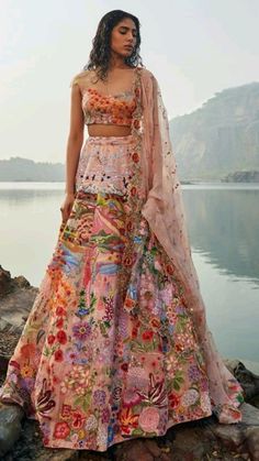 a woman standing on top of a rock next to a lake wearing a colorful dress