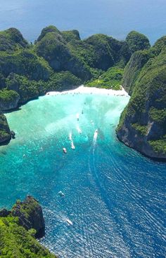 an aerial view of several boats in the water near some rocks and green vegetation, surrounded by blue water