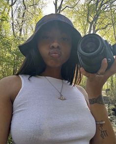 a woman holding up a camera in front of her face and wearing a hat on top of her head