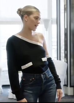 a woman standing in front of a window wearing jeans and a black top with white trim