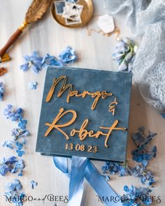 a blue and gold wedding sign on a table surrounded by flowers, feathers and lace