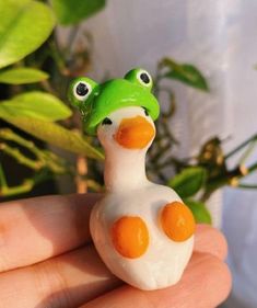 a hand holding a small toy duck in it's left hand, next to a potted plant