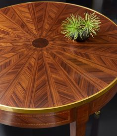 a round wooden table with a plant on it's top and gold trim around the edge