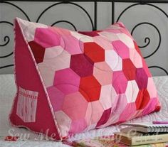 a pink and red pillow sitting on top of a bed next to a pile of books