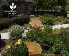 a garden with flowers and rocks in front of a brick building that says central texas gardener