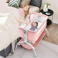 a woman holding a baby in a pink crib next to a bed and nightstand