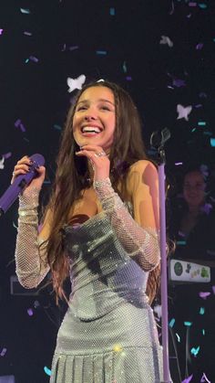 a woman singing into a microphone with confetti in the air above her head