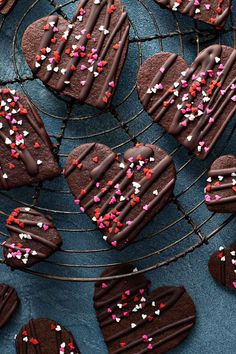 heart shaped cookies with chocolate frosting and sprinkles on a wire rack