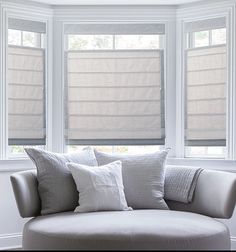 a white couch sitting in front of two windows with blinds on them and pillows on the back