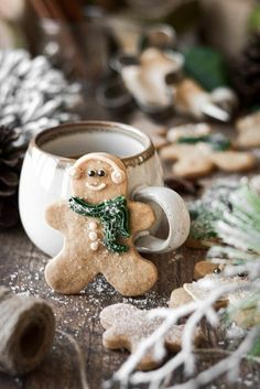 a gingerbread man in a green scarf is next to a cup of coffee and pine cones