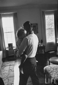 a black and white photo of a man holding a child in his arms while standing in a living room