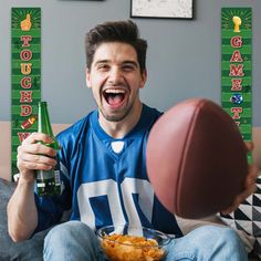 a man sitting on a couch holding up two beer bottles and a football in front of him