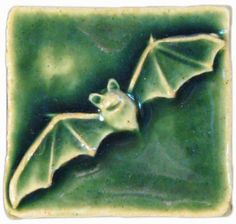 a green ceramic tile with a bat on it's back and its wings spread out