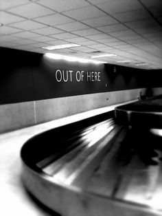 a sign that says out of here in front of an escalator at the airport