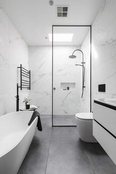 a white bathroom with black accents and marble walls, along with a free standing tub