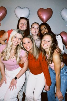 a group of young women standing next to each other in front of heart shaped balloons