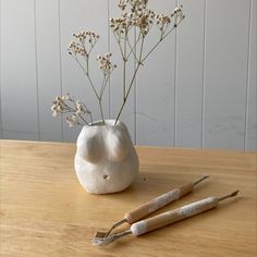 two white vases with flowers in them sitting on a table next to utensils