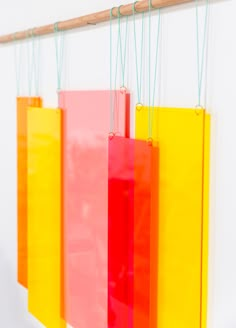 three colorful bags hanging on a wall with string attached to them and two wooden pegs in the background